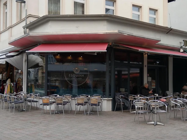 Außenbereich des Esquina Café & Bar mit roten Markisen und Tischen in der Fußgängerzone
