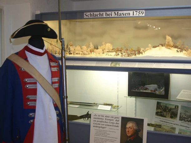 Diorama im Heimatmuseum Maxen Mannequin in historischer Uniform mit Dreispitz vor einem Diorama der Schlacht bei Maxen 1759, umgeben von Infotafeln und Bildern.