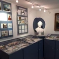 Serre-Raum im Heimatmuseum Maxen Ein kleiner Ausstellungsraum mit blauen Vitrinen, einer weißen Büste, gerahmten Bildern und Dokumenten an den Wänden, in heller Beleuchtung.