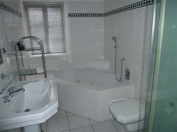 Das Badezimmer - Wohnung Helles, modern gefliestes Badezimmer mit Badewanne, separater Dusche, Waschtisch und WC. Ein Fenster mit Jalousien lässt Tageslicht herein, während verchromte Armaturen und Ablagen für einen gepflegten Eindruck sorgen. Der Raum bietet viel Komfort für einen entspannten Aufenthalt auf dem Land.