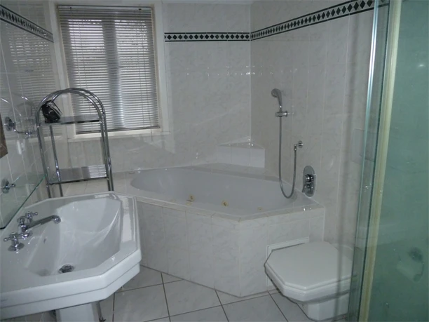Das Badezimmer - Wohnung 4.JPG Helles, modern gefliestes Badezimmer mit Badewanne, separater Dusche, Waschtisch und WC. Ein Fenster mit Jalousien lässt Tageslicht herein, während verchromte Armaturen und Ablagen für einen gepflegten Eindruck sorgen. Der Raum bietet viel Komfort für einen entspannten Aufenthalt auf dem Land.