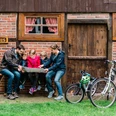 Eine Familie sitzt vor einem Backhaus auf einer Bank, betrachtet eine Landkarte; zwei Fahrräder stehen daneben.
