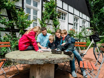Familientreffen auf steinernem Tisch: Eine Gruppe erkundet entspannt eine Landkarte im Freien.