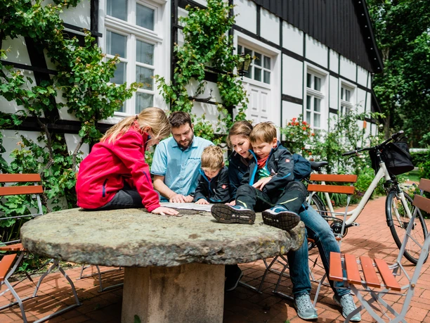 Thorsten-Hennig-Fotografie-Fahrradtouren-Hövelhof-2019-A9_06270.jpg Familientreffen auf steinernem Tisch: Eine Gruppe erkundet entspannt eine Landkarte im Freien.