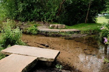 Bachgabelung mit Bruchsteinbrücken, umgeben von üppigem Grün, ruhiger Natur und fließendem Wasser.