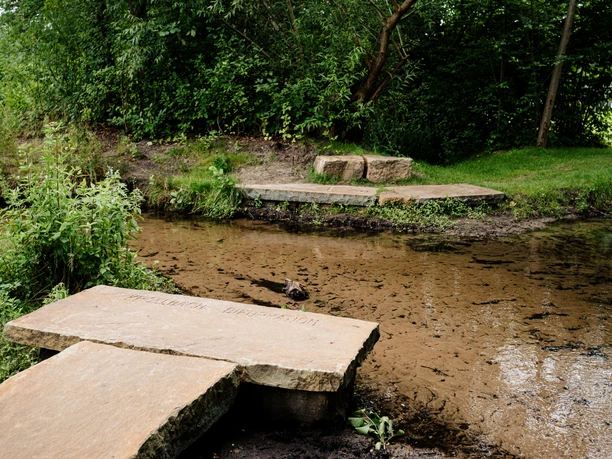 Bifurkation Hövelhof Bachgabelung mit Bruchsteinbrücken, umgeben von üppigem Grün, ruhiger Natur und fließendem Wasser.