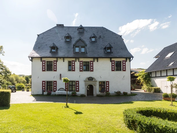 Malteser Komturei <p>Historisches weißes Fachwerkhaus mit Schieferdach, vor grünem Rasen und blauen Himmel in Bergisch Gladbach.</p>