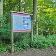 Waldweg im Wiehengebirge mit einem Infokasten zur Orientierung, umgeben von dichtem Laubwerk.