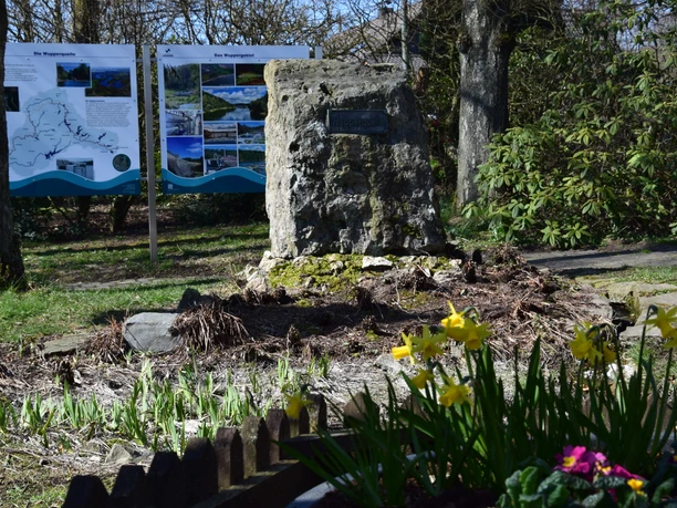 Wupperquelle <p>Steinmonument in einem Park mit Infotafeln im Hintergrund und blühenden Narzissen im Vordergrund.</p>