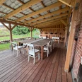 lebensrau-kräuter-amelinghausen1.JPG Überdachte Holzterrasse mit langem Holztisch und weißen Stühlen an einem Backsteingebäude.