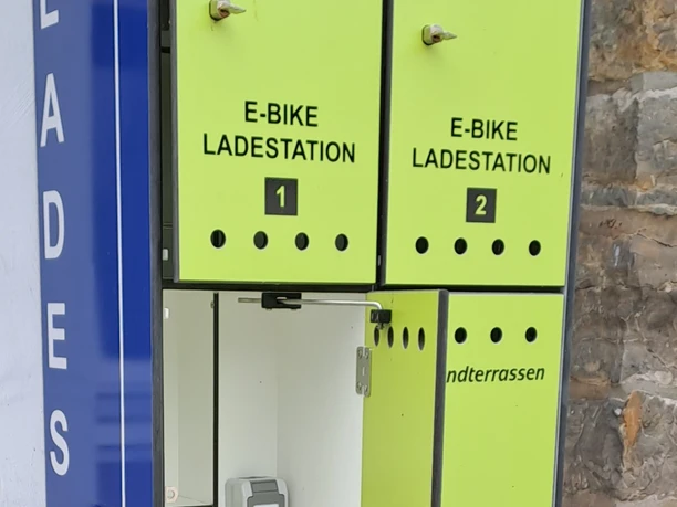 Ein E-Bike-Ladestation mit vier Schließfächern, integriert in eine Steinwand, bietet praktischen Zugang.