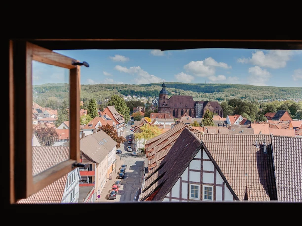 Einbeck überblicken! Ausblick durch ein offenes Fenster auf Einbecks Altstadt mit Fachwerkhäusern und Kirche.