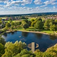 Blick auf einen bewaldeten See mit Steg inmitten einer grünen Landschaft und vereinzelten Häusern.View of a wooded lake with a jetty in the middle of a green landscape and scattered houses.Udsigt over en skovklædt sø med en badebro midt i et grønt landskab med spredte huse.Uitzicht op een bebost meer met een steiger in het midden van een groen landschap en verspreide huizen.
