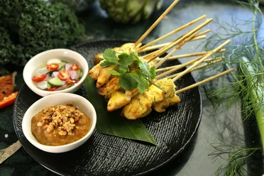 satay-chicken-pixabay.jpg Gegrillte Hühnchenspieße auf schwarzem Teller, serviert mit würziger Erdnuss- und Gurken-Chili-Sauce.
