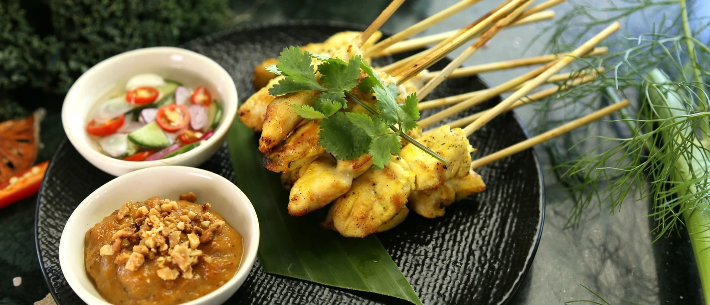 satay-chicken-pixabay.jpg Gegrillte Hühnchenspieße auf schwarzem Teller, serviert mit würziger Erdnuss- und Gurken-Chili-Sauce.