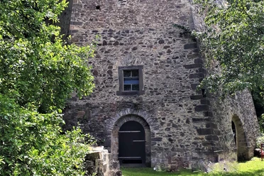 Historic lime kiln 1856 Stone wall of an old building with a small window and a wooden door, surrounded by green trees and grass.