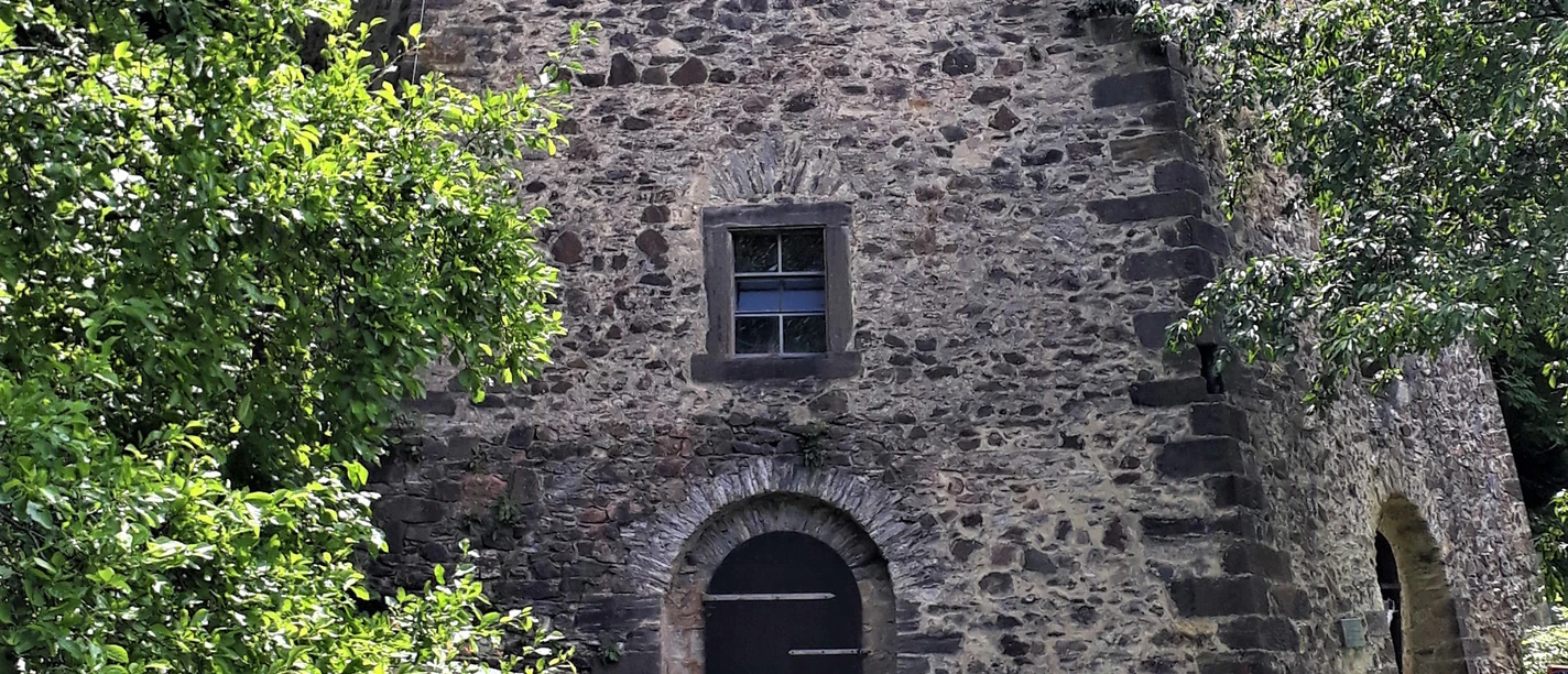 Historic lime kiln 1856 Stone wall of an old building with a small window and a wooden door, surrounded by green trees and grass.