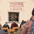 Fenstermusik Personen sitzen im Freien und lauschen einem Musiker, der aus einem Fenster heraus spielt.