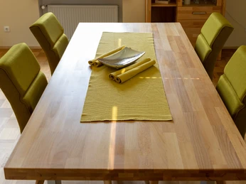 Moderner Essbereich mit Holztisch, grünen Stühlen und gelbem Läufer, warm beleuchtet durch Sonnenlicht.