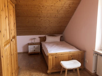 Termuende4 Schlafzimmer1.jpg Schlafzimmer mit Einzelbett unter Dachschräge, aus Holz gefertigt, mit Nachttisch und Hocker.