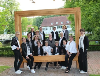 Der Gospelchor Lunedi Sera posiert in schwarz-weißer Kleidung vor einem großen Holzrahmen im Freien.