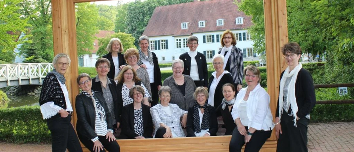 Gospelchor Lunedi Sera Der Gospelchor Lunedi Sera posiert in schwarz-weißer Kleidung vor einem großen Holzrahmen im Freien.