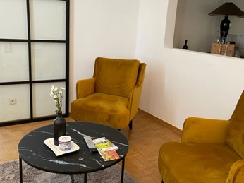 Zwei senfgelbe Sessel stehen um einen runden Tisch auf einem Teppich in einer modern eingerichteten Ecke.