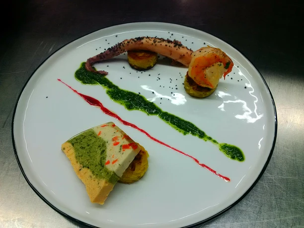 Ein kunstvoll angerichteter Teller mit Meeresfrüchten, gewürzt mit farbigen Saucen, auf dunkler Platte.