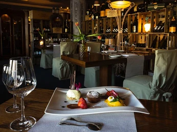 Hotel Westhoff_CCBYSA_Teutoburger Wald_Stadt_Schloss_Holte-Stukenbrock_Hotel Westhoff (9).jpg Gedeckter Tisch in einem stilvollen Restaurant mit Weinregalen und eleganten Desserts.