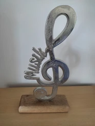 Skulptur eines Violinschlüssels mit leicht schimmernder Oberfläche, stehend auf Holzsockel.