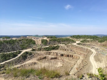 Blick in den Steinbruch Steinbruch bei Lindlar: Weite Landschaft mit unbefestigten Wegen, umgeben von grün bewachsenen Hügeln.