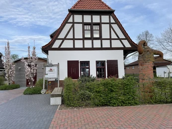 Ehemaliges Bahnhofsgebäude mit Fachwerk und rotem Ziegeldach, umgeben von blühenden Bäumen.