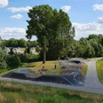 Pumptrack Rheda-Wiedenbrück Eine grüne Landschaft mit einem hügeligen Pumptrack, umgeben von Bäumen und Menschen, die Rad fahren.