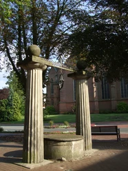 S 0019.JPG Steinbrunnen mit zwei Säulen und verziertem Eisenaufsatz vor roter Backsteinkirche in Sögel