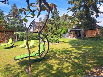 Freihängende Loungesessel und Liegestühle auf einer grünen Wiese, umgeben von Bäumen und Sträuchern.