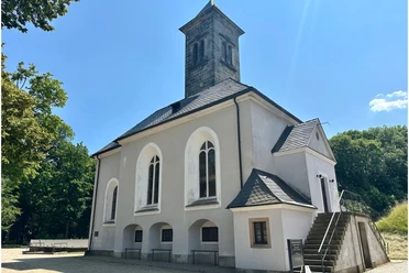 Garnisionskirche auf der Festung Königstein White church with gray tower and pointed roof, surrounded by trees under a clear blue sky; quiet, sunny atmosphere.