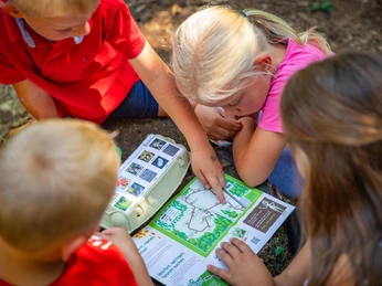Frerener Holtpättken ©Emsland Tourismus GmbH Kinder sitzen auf dem Waldboden und entdecken gemeinsam ein buntes Naturerlebnisheft.