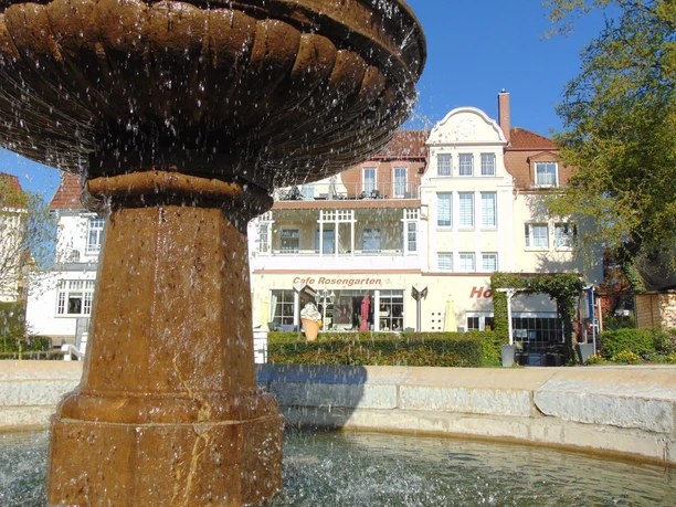 Brunnen im Vordergrund, dahinter die helle Fassade des Hotel & Cafe Rosengarten