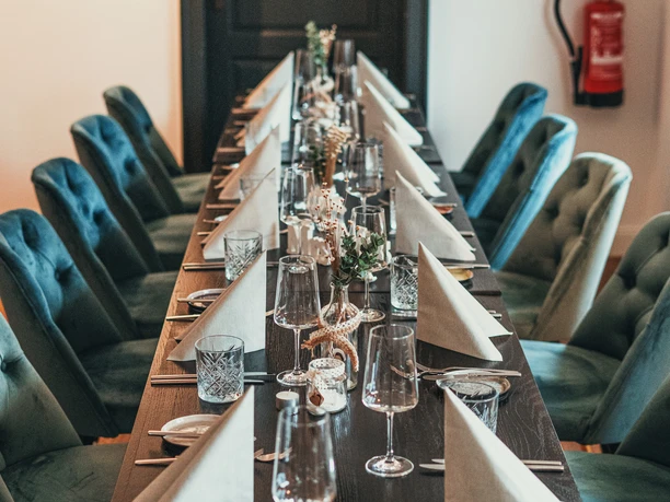 ManuFaktur Speisekarte Herbst 2021.jpg Festlich gedeckter Tisch mit weißem Geschirr, Gläsern und gefalteten Servietten, dekoriert für ein elegantes Dinner.