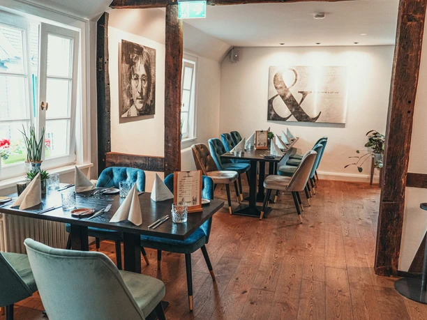 ManuFaktur Speisekarte Herbst 2021-69.jpg Gemütlicher Gastraum in einem Restaurant mit Holzboden, modernen Bildern und stilvollen Sitzmöbeln.