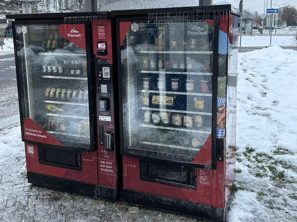 Dva červené automaty venku, pokryté ledem a sněhem, nabízejí občerstvení a nápoje. Zimní, mrazivá atmosféra.