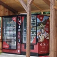 Proviantomat in Pfaffendorf Roter Verkaufsautomat mit Snacks und Getränken unter einem hölzernen Unterstand, umgeben von ländlicher Umgebung.Red vending machine with snacks and drinks under a wooden shelter, surrounded by rural surroundings.Červený automat s občerstvením a nápoji pod dřevěným přístřeškem, obklopený venkovským prostředím.Czerwony automat z przekąskami i napojami pod drewnianą wiatą, w otoczeniu wiejskiej przyrody.Rode automaat met hapjes en drankjes onder een houten afdak, omgeven door een landelijke omgeving.Distributore automatico rosso con snack e bevande sotto una tettoia in legno, circondato da un ambiente rurale.