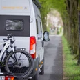 Wohnmobilstellplätze im Osnabrücker Land Ein Wohnmobil mit Fahrradträger fährt auf einer von Bäumen gesäumten Landstraße entlang.