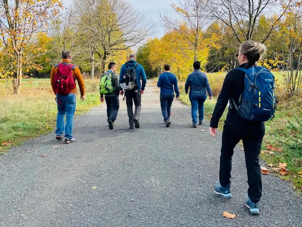Hike with Elke Wolf Six people with rucksacks hike along an autumnal path surrounded by trees with yellow leaves.