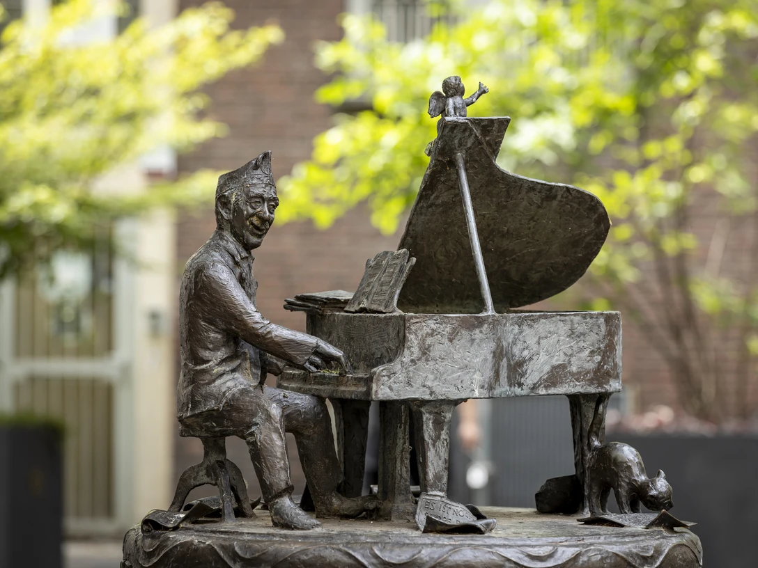 Jupp Schmitz memorial Skulptur von Jupp Schmitz am Klavier, umgeben von Bäumen.Sculpture of Jupp Schmitz at the piano, surrounded by trees.