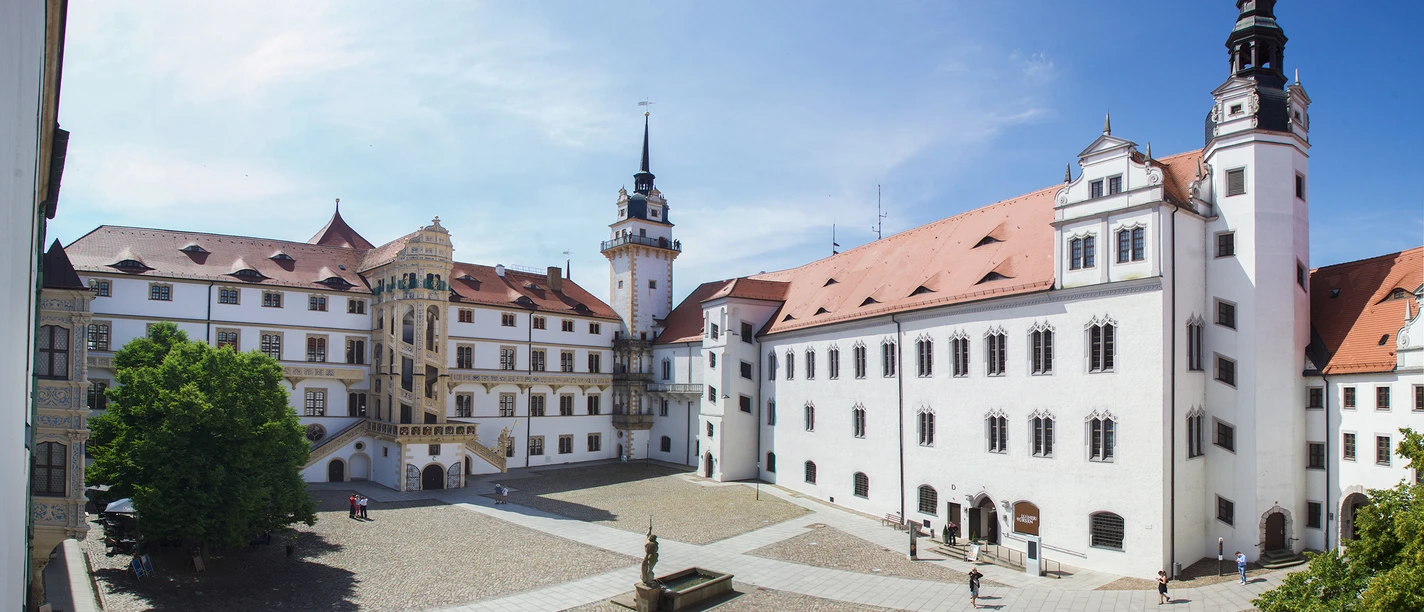 Schloss-Hartenfels-Innenhof-Foto-A-Kloeppel.jpg Heller Schlossinnenhof mit umliegenden, historischen Gebäuden und einer zentralen Brunneninstallation.