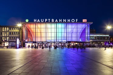 Köln Hauptbahnhof Der Eingang des Kölner Hauptbahnhofs bei Nacht, beleuchtet in Regenbogenfarben.