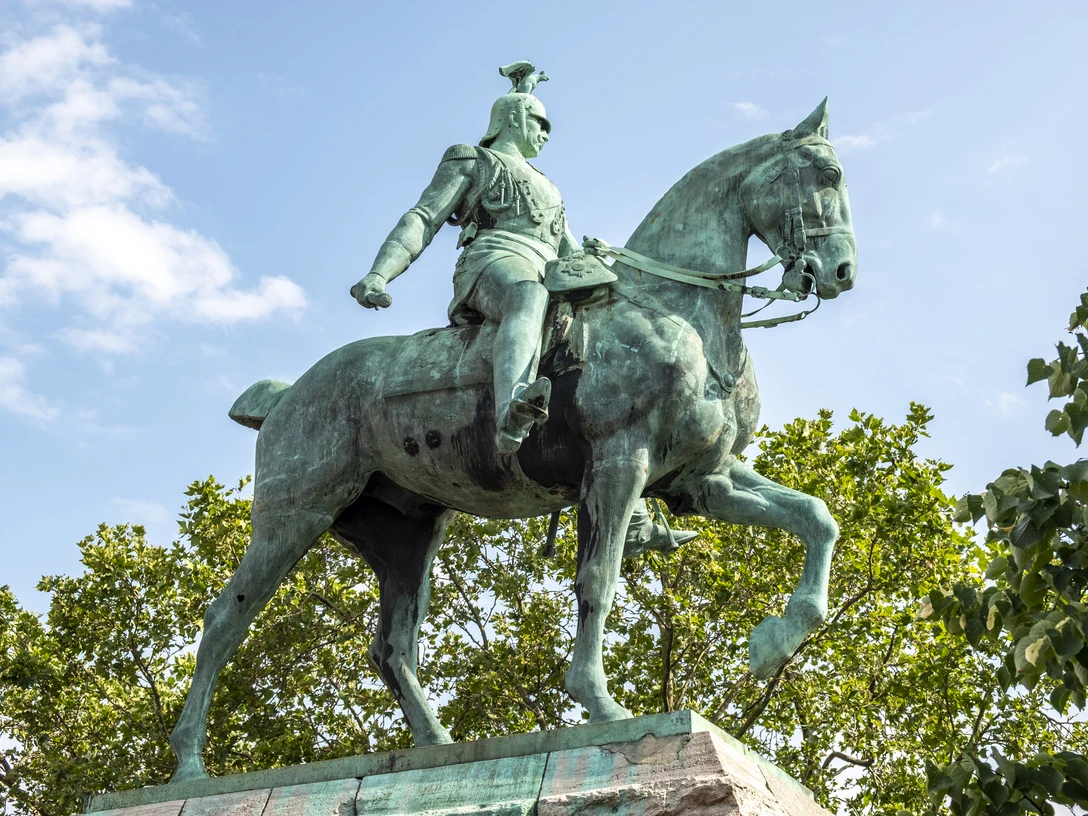 Reiterstandbild König Friedrich Wilhelm III. Das Bild zeigt das beeindruckende Reiterstandbild von Kaiser Wilhelm II. in Köln. Kaiser Wilhelm sitzt majestätisch auf einem kräftigen Pferd, umgeben von grünen Bäumen und einem klaren, blauen Himmel im Hintergrund. The picture shows the impressive equestrian statue of Kaiser Wilhelm II in Cologne. Kaiser Wilhelm sits majestically on a powerful horse, surrounded by green trees and a clear blue sky in the background.