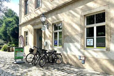 Fietsstation voor een historisch gebouw met verschillende geparkeerde fietsen, borden en een groen bord op kasseien.
