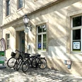Fahrradstation Pirna Fahrradstation vor einem historischen Gebäude mit mehreren geparkten Fahrrädern, Schildern und einem grünen Hinweisschild auf Kopfsteinpflaster.